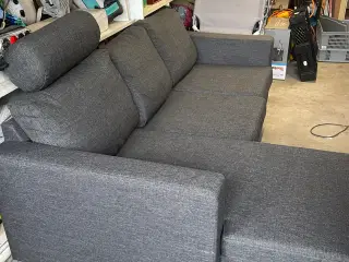 Grå sofa i stof med chaiselong. 