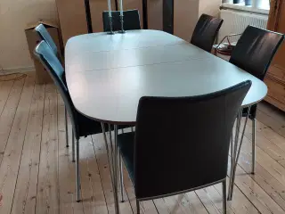 Gråt spisebord. 2 tillægsplader. 6 sorte læderstol
